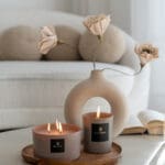 luxury-scented-candle-sand-collection-lit0up-satin-taupe-mocca-glass-vessel-mocca-taupe-wax-on-a-coffee-table-luxury-steeing-with-vase