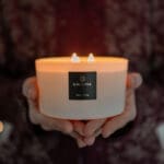 Beautiful noel noel white 3 wick candle offered as gift, held in hands