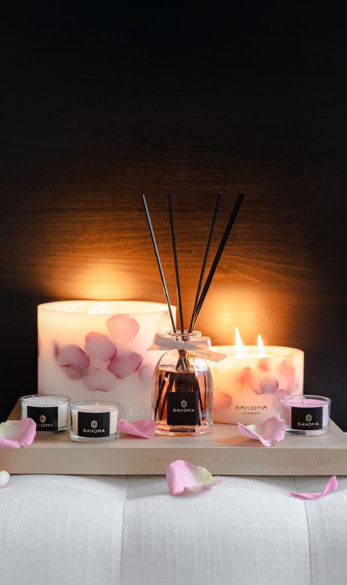Velvet Rose Botanical Pillar candles made with real rose petals, octagonal diffuser and three candles from Nine Lights Candle Set arranged on a tray in a romantic display with dark background and glow
