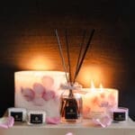 Velvet Rose Botanical Pillar candles made with real rose petals, octagonal diffuser and three candles from Nine Lights Candle Set arranged on a tray in a romantic display with dark background and glow
