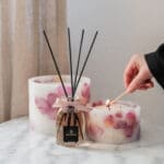 A hand lighting up Velvet Rose pillar candles with a octagonal diffuser in same fragrance