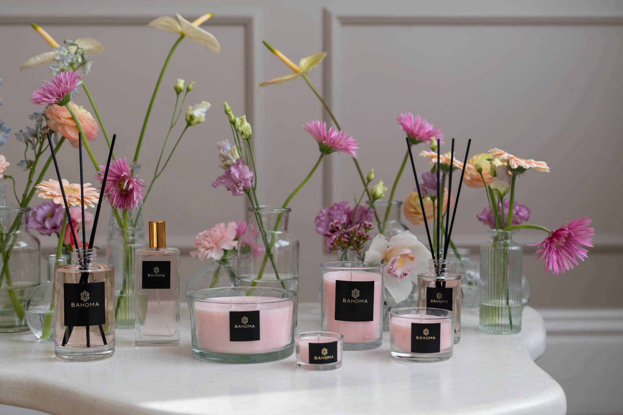 Velvet Peony & Cashmere – Set of 3 Compact Candles | Alchemy Collection. A lifestyle display of full fragrance family with light pastel pink candles and light pastel pink diffuser and room spray liquid.