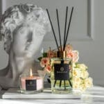 primrose-and-amberwood-200ml-fragranced-diffuser-alchemy-with-a-compact-candle-and-clay-bust-with-a-vase-and-flowers-in-the-background